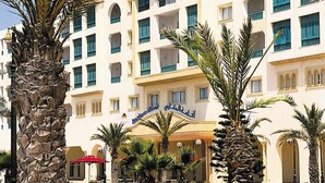 Un hôtel à plusieurs étages, doté d’une entrée principale, de palmiers et de balcons.