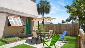Een terras met een tafel en stoelen, een houten hek en een palmboom op de achtergrond.