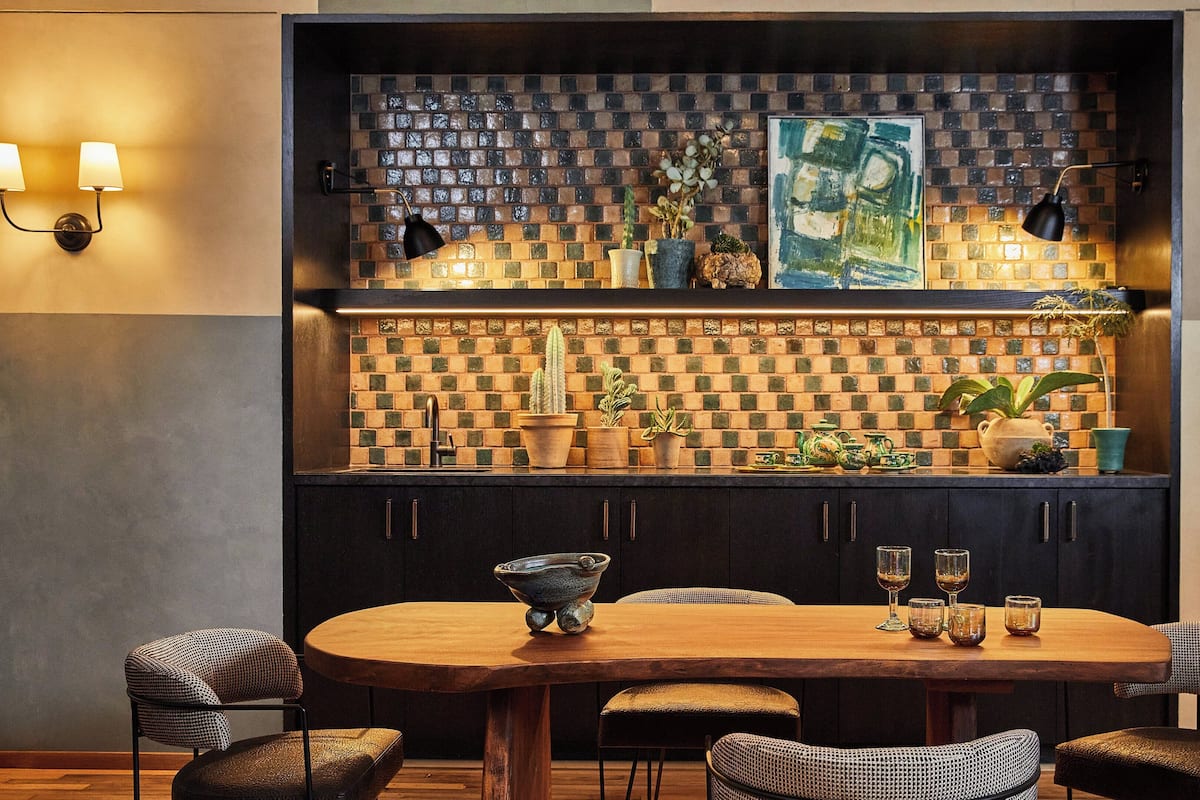 A modern kitchen with a checkered backsplash, dark cabinets, and a wooden dining table with four chairs.