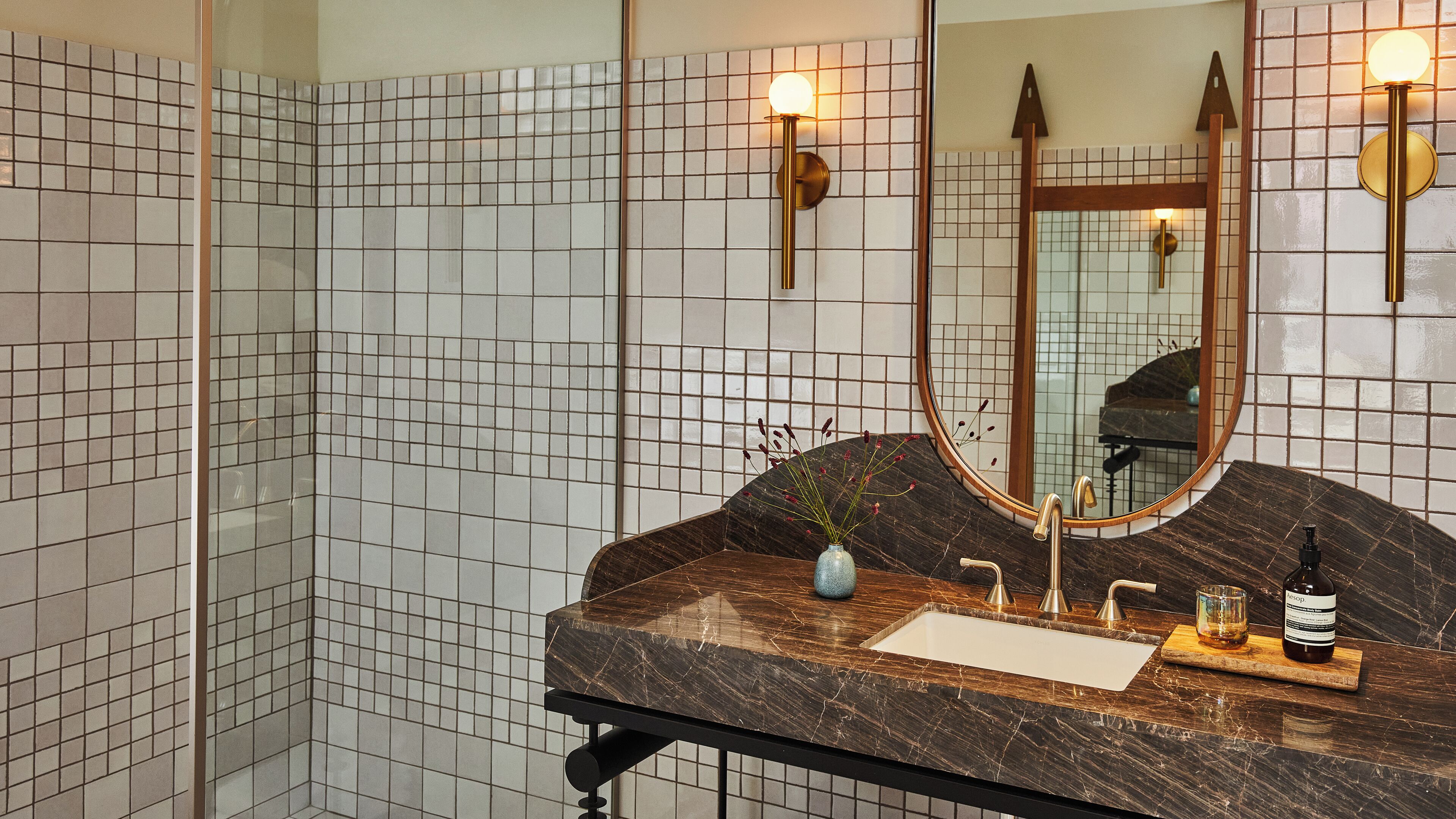 Une salle de bain avec un lavabo en marbre, un miroir et un mur recouvert de petits carreaux.