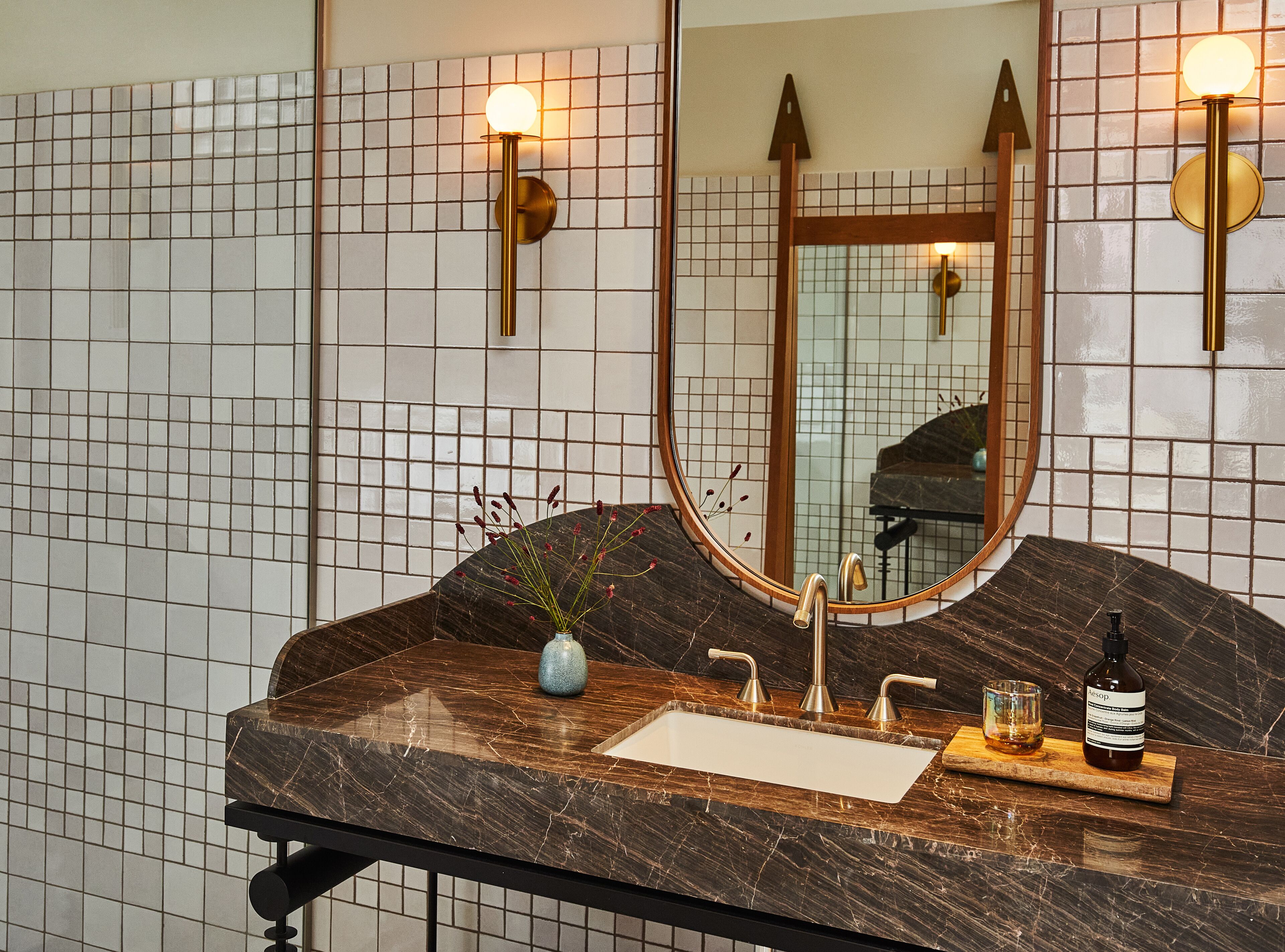 Un baño con lavamanos de mármol, un espejo y un florero con plantas.