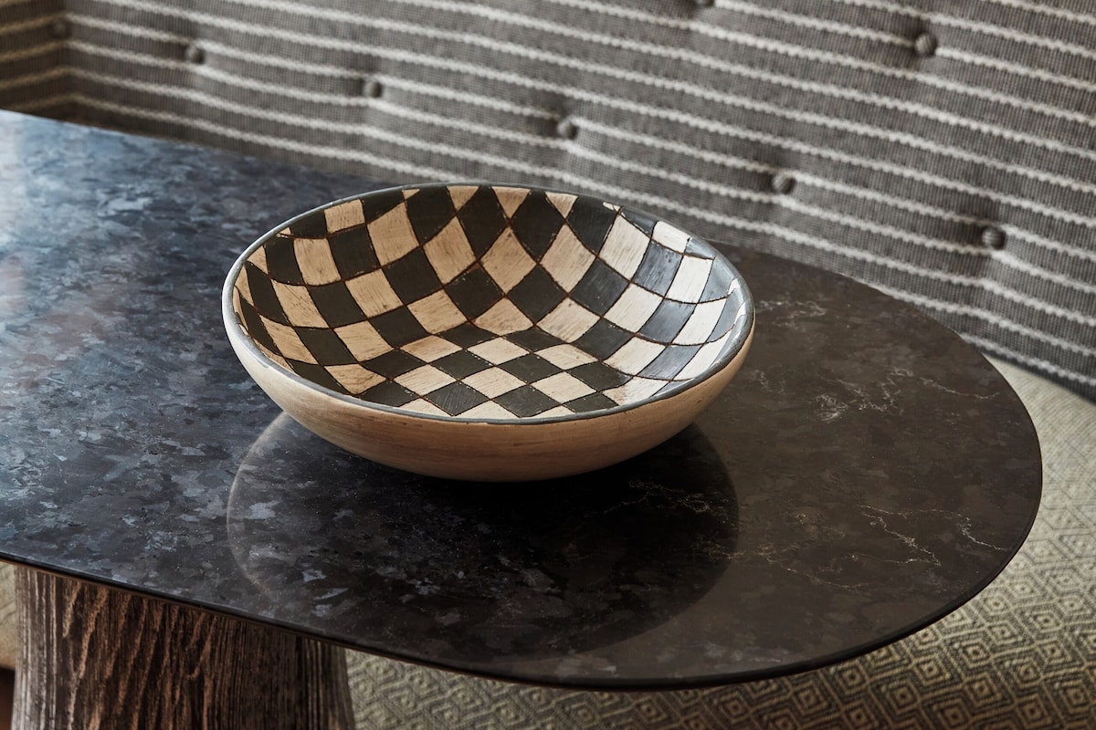A bowl on a round table in a room with a bed and a patterned sofa.
