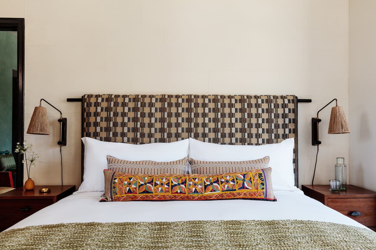 A neatly made bed with a patterned headboard, two bedside lamps, and a vase with flowers on a nightstand.