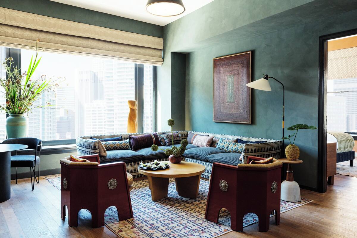 A modern living room with a sofa, coffee table, and chairs. There is a large window with a view of buildings.