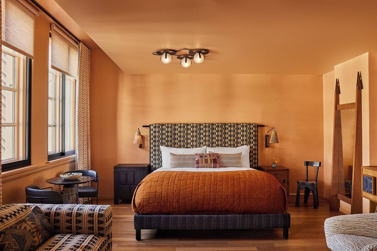 A bedroom with a large bed, a small table, two chairs, a nightstand, and a mirror.