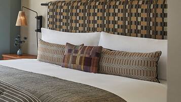 Cama bem arrumada com roupa de cama estampada, abajur e cabeceira fixada na parede.