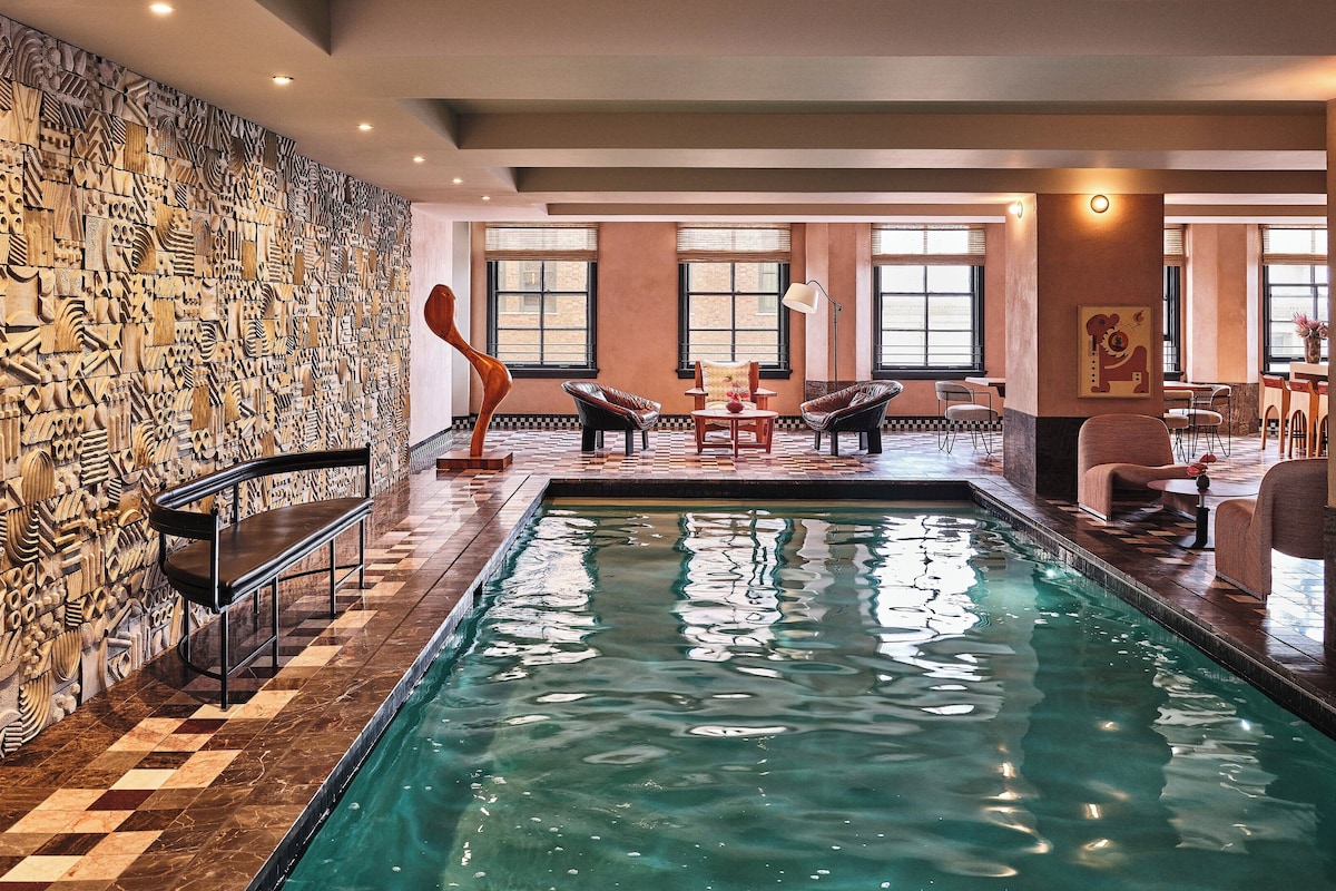 A swimming pool with a checkered floor, surrounded by lounge chairs and a wall with intricate carvings.