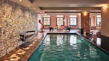 A swimming pool with a checkered floor, surrounded by lounge chairs and a wall with intricate carvings.