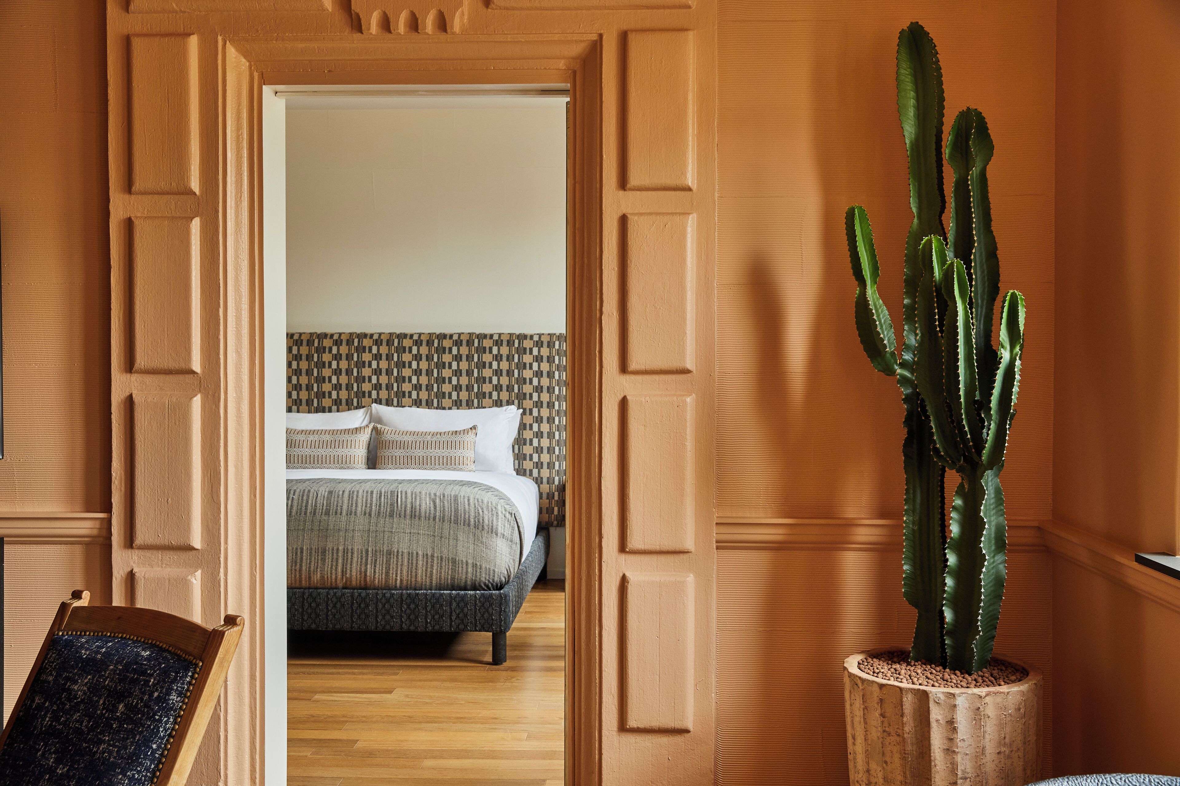 A doorway leading to a bedroom with a bed, a potted cactus, and a wooden chair.