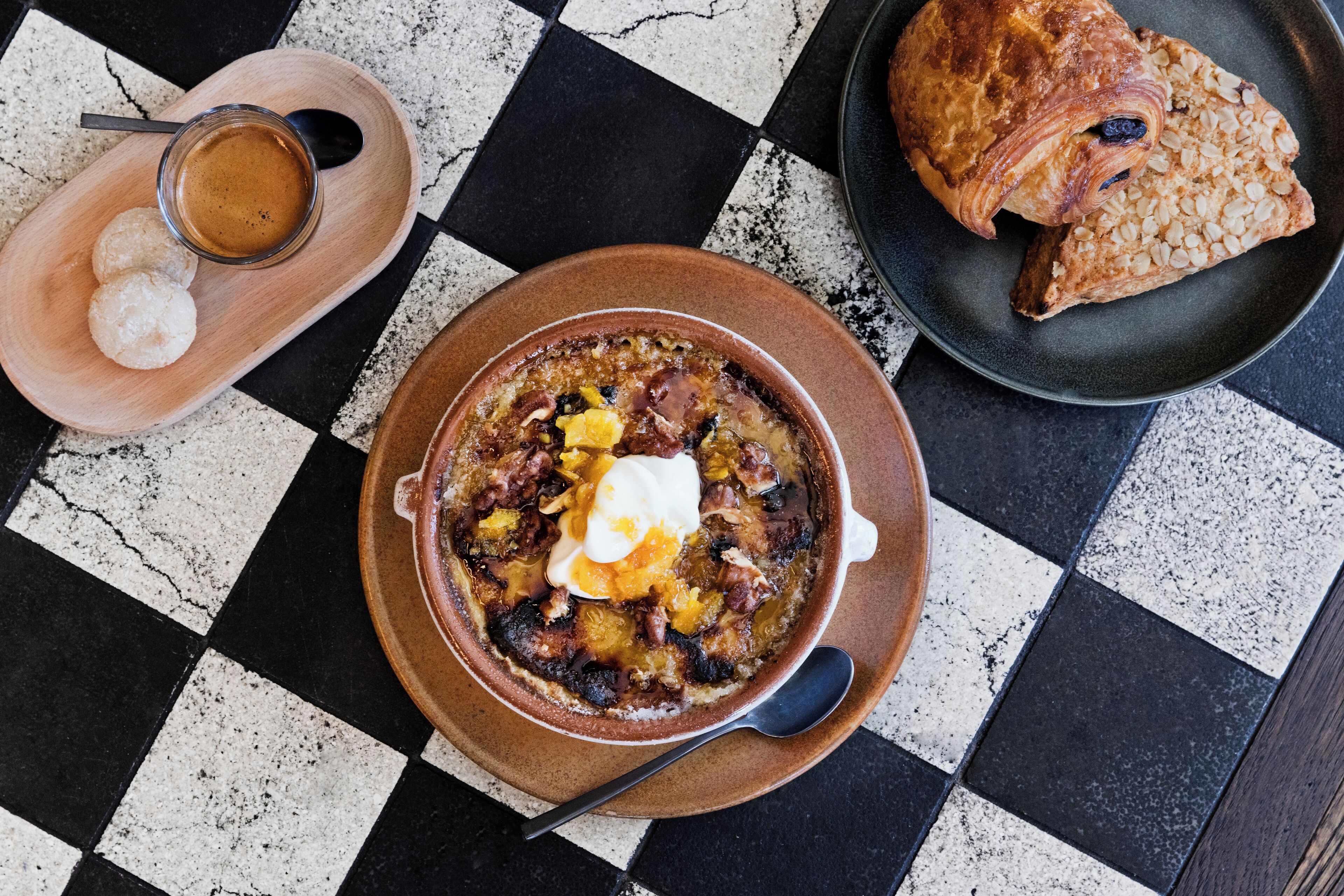 A checkered table with a bowl of soup, a croissant, and a cup of coffee.