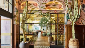 Un hall d’entrée spacieux, doté d’un sol à carreaux, de grands cactus en pot et offrant une vue sur un espace de restauration avec des tables et des chaises.