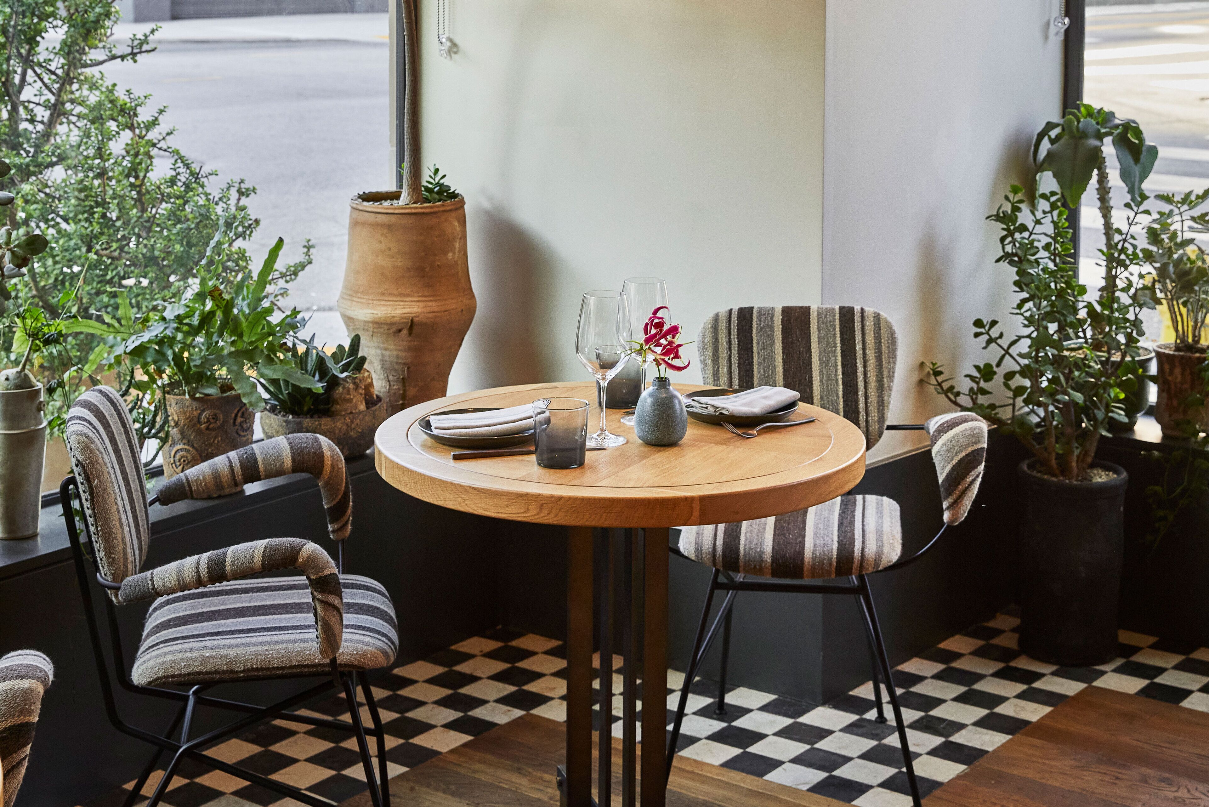 Un comedor acogedor con una mesa redonda de madera, sillas tapizadas a rayas y plantas en macetas.