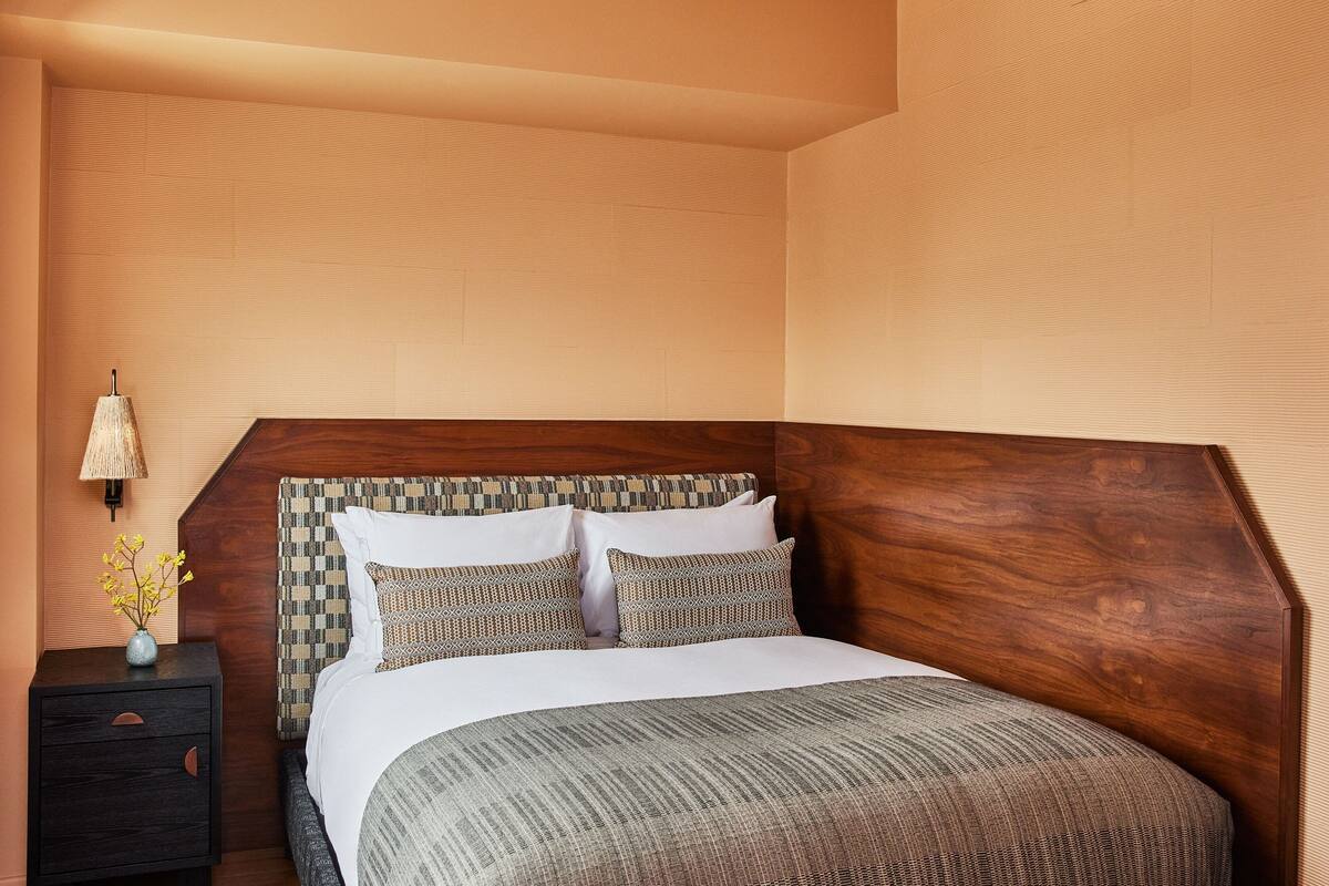 A neatly made bed with a wooden headboard, a bedside table with a lamp, and a vase with flowers.