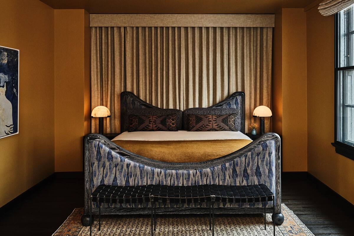 A bed with patterned headboard and footboard, two bedside lamps, and a large window with curtains.