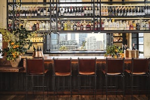 A bar with multiple shelves of bottles, a large window with a city view, and several chairs. - Downtown Los Angeles Proper Hotel, a Member of Design Hotels (Los Angeles)