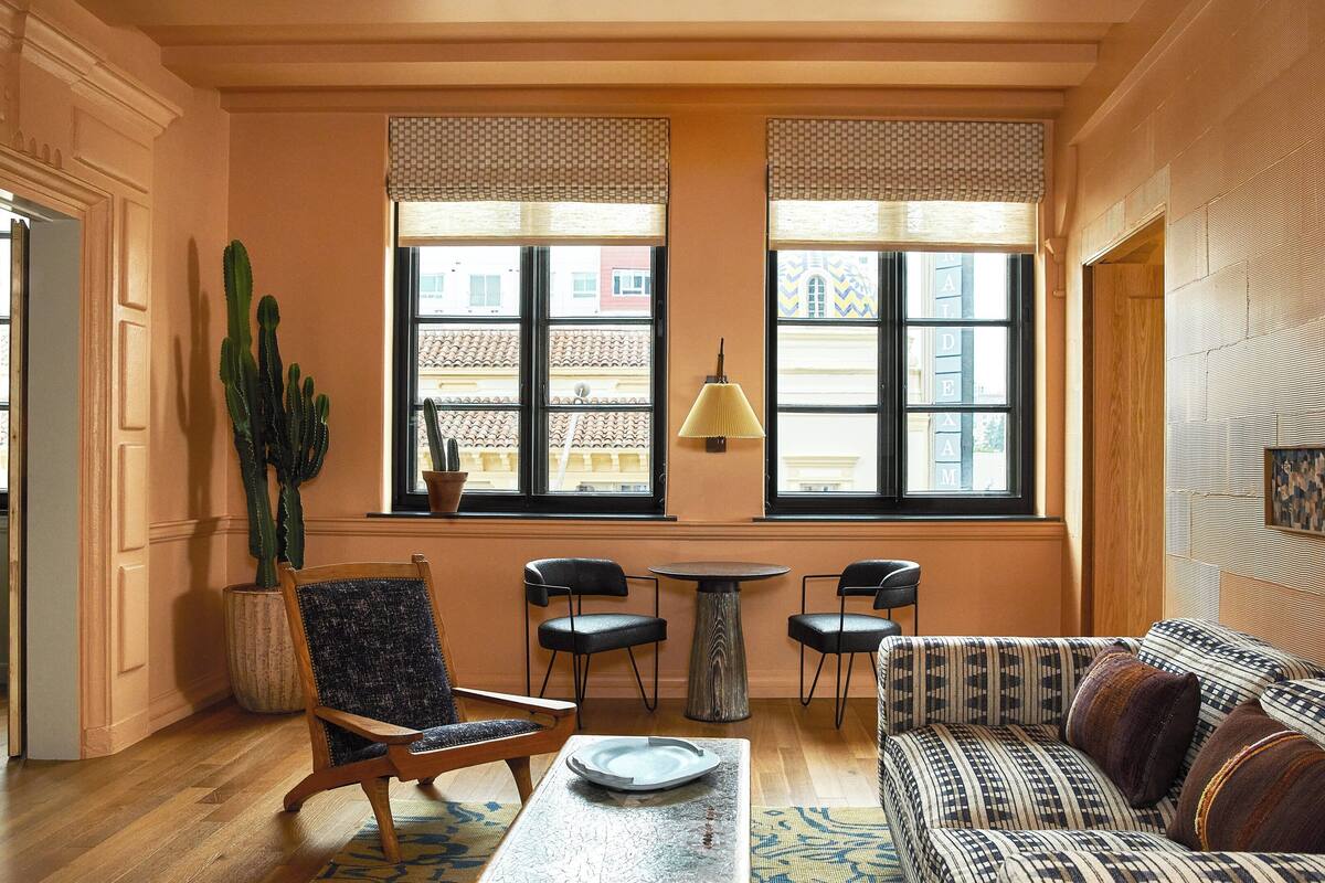A cozy room with a wooden floor, a patterned sofa, a cactus plant, and a table with chairs.