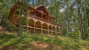 A wooden cabin with a balcony, surrounded by dense forest.