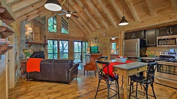L’intérieur chaleureux d’un chalet avec un plafond en bois, un coin repas comprenant une table et des chaises, un canapé et une cuisine équipée.