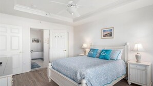 Ein Schlafzimmer mit einem Bett, zwei Nachttischen mit Lampen, einem Deckenventilator und einer Tür zu einem Badezimmer.