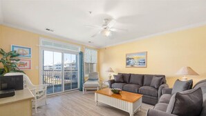 Ein Wohnzimmer mit grauem Sofa, einem weißen Couchtisch und einem Balkon mit Blick auf Gebäude.