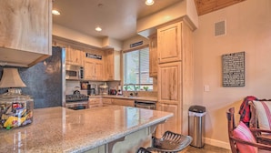 A kitchen with wooden cabinets, a granite countertop, a stainless steel refrigerator, a microwave, a stove, and a sink. There is a trash can and a chair in the corner. - Mammoth Lakes Townhome - 10-Min Walk to Village! (Mammoth Lakes)