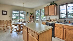 A kitchen with wooden cabinets, a dishwasher, and a large island. There is a dining area with chairs and a table.