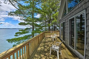 A wooden deck with a railing overlooking a body of water, two white chairs, and large windows. - St Lawrence Waterfront Home w/ Grill and Deck! (Hammond)