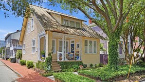 Une maison jaune avec un porche, un petit jardin et un arbre devant.
