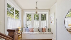 Une pièce dotée d’une banquette intégrée, d’un lustre et d’une fenêtre ornée de vitraux offrant une vue sur l’extérieur.