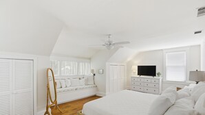 Une chambre à coucher comprenant un lit, une commode, un téléviseur, une fenêtre avec des stores et un ventilateur de plafond.