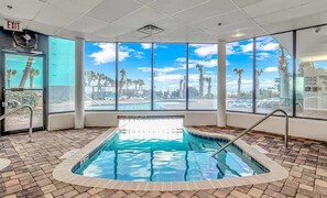 Zona de piscina con vistas despejadas a palmeras y un cielo azul a través de amplios ventanales.