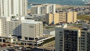 A high-rise hotel with multiple floors, a parking lot, and a view of the ocean.
