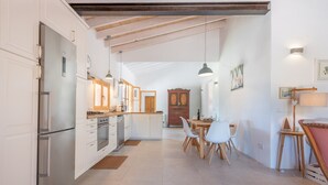 Una cocina moderna con armarios blancos, electrodomésticos de acero inoxidable y un comedor con sillas blancas y una mesa de madera.