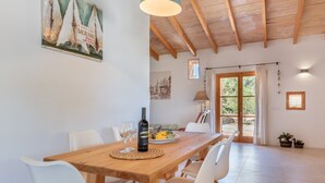 Un comedor con una mesa de madera, sillas blancas, una botella de vino y un plato de fruta.