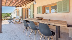 Un área de comedor al aire libre con mesa y sillas de madera, una pérgola en la parte superior y vista a un jardín.