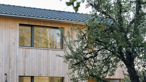 Ett modernt trähus med stora fönster och en matplats som syns genom glasdörrarna.
