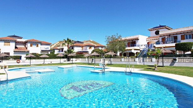 A swimming pool surrounded by buildings with balconies and a clear blue sky. - VM 6 - Duplex with private garden near the beach (Vera playa)
