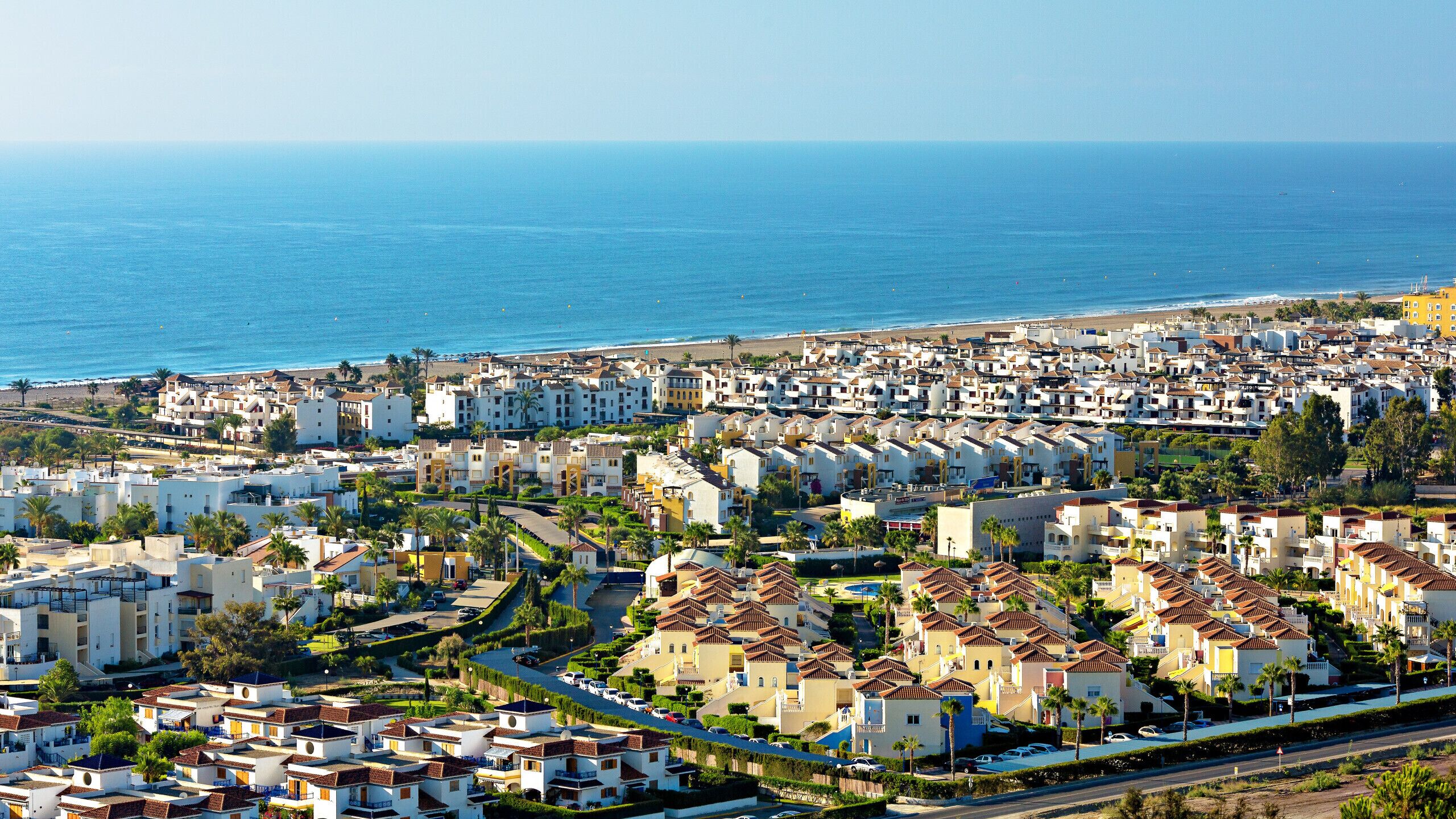 A coastal residential area with buildings, a beach, and a clear view of the sea.