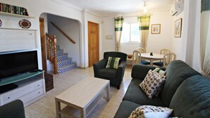 A living room with a sofa, armchair, coffee table, TV, staircase, and a dining area with chairs and a table. - VM 6 - Duplex with private garden near the beach (Vera playa)