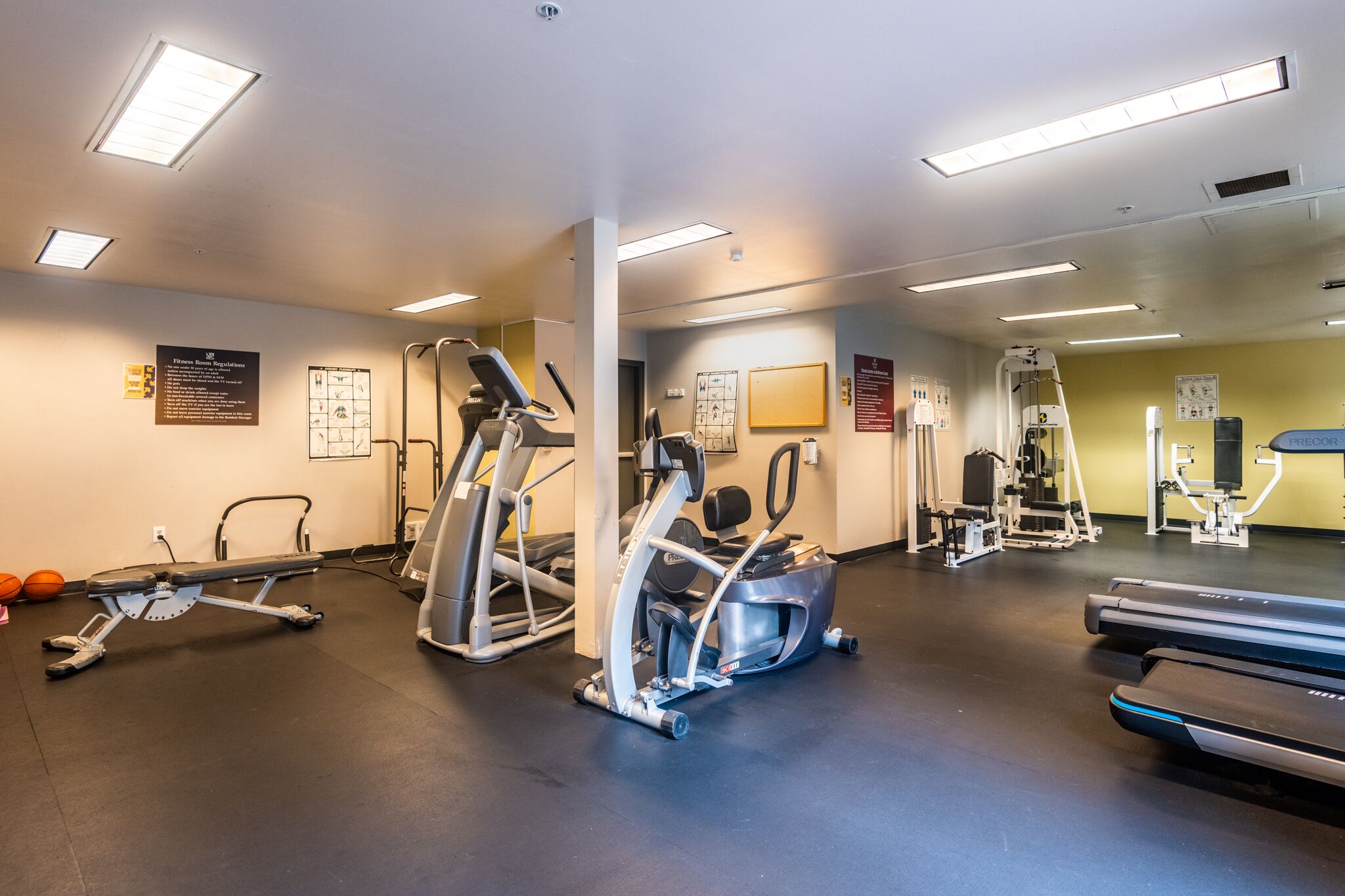 Une salle de sport équipée de divers appareils d’exercice, notamment des tapis de course et des appareils de musculation, et dotée d’un mur recouvert de miroirs.