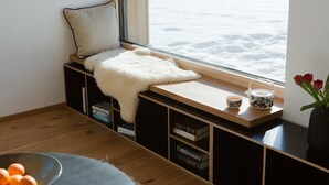 Eine gemütliche Leseecke mit einer gepolsterten Bank, einem kleinen Tisch mit Teekanne und Tasse sowie Blick auf eine verschneite Landschaft.