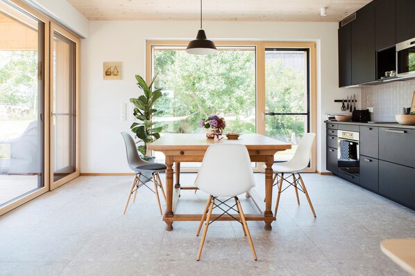 A modern kitchen with a wooden dining table, white chairs, and a large window.