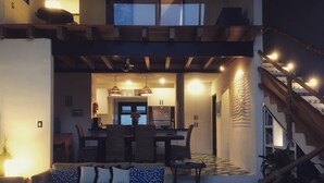 Uma sala de estar moderna com sofá, mesa de centro e área de jantar com cadeiras e mesa. Uma escada com corrimão de madeira leva a um andar superior.