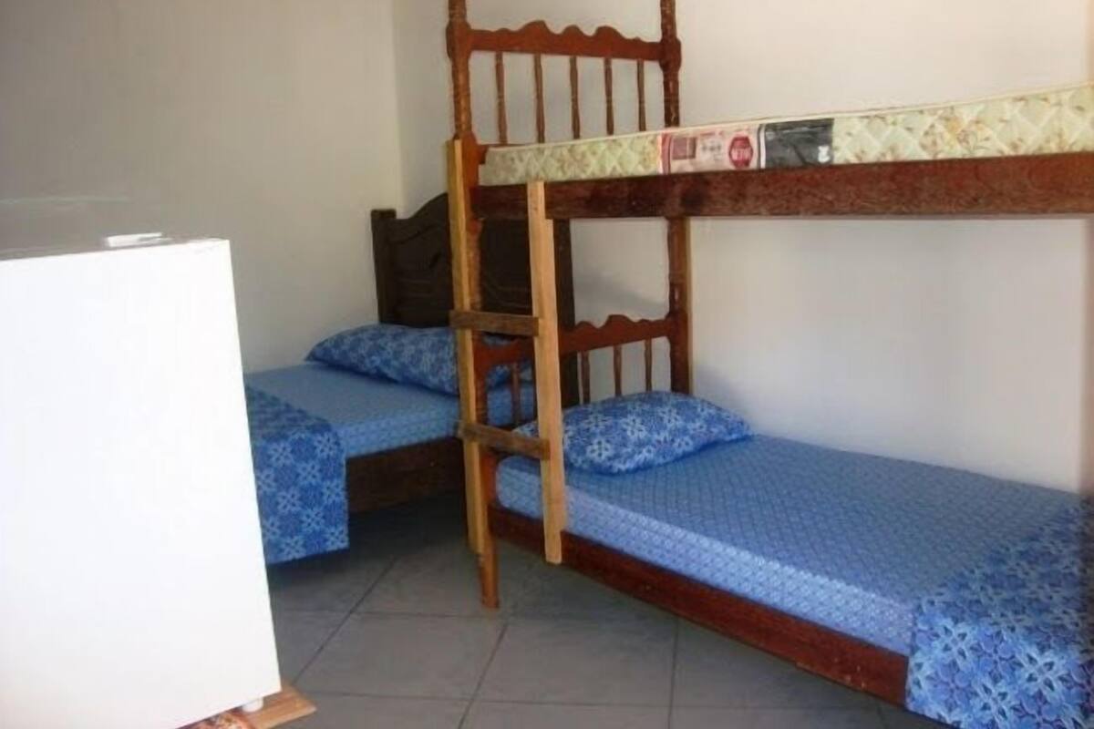 A bunk bed room with a wooden ladder, two beds with blue patterned bedding, and a white refrigerator.