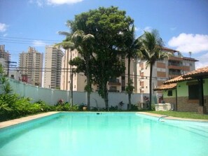 Una piscina con vistas a edificios residenciales altos y un gran árbol al fondo.