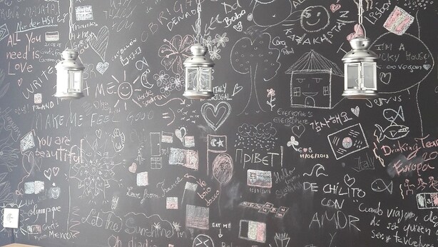 A bar area with a blackboard wall featuring various doodles and writings, including a lantern hanging from the ceiling. - Timor Guest House (Lisbon)