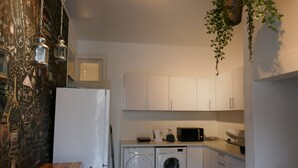 A compact kitchen with a washing machine, microwave, and white cabinets. - Timor Guest House (Lisbon)