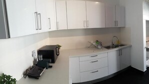 A compact kitchen with white cabinets, a sink, and a stove. - Timor Guest House (Lisbon)