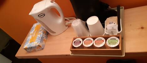 A coffee station with a coffee maker, disposable cups, and a tray of coffee pods.