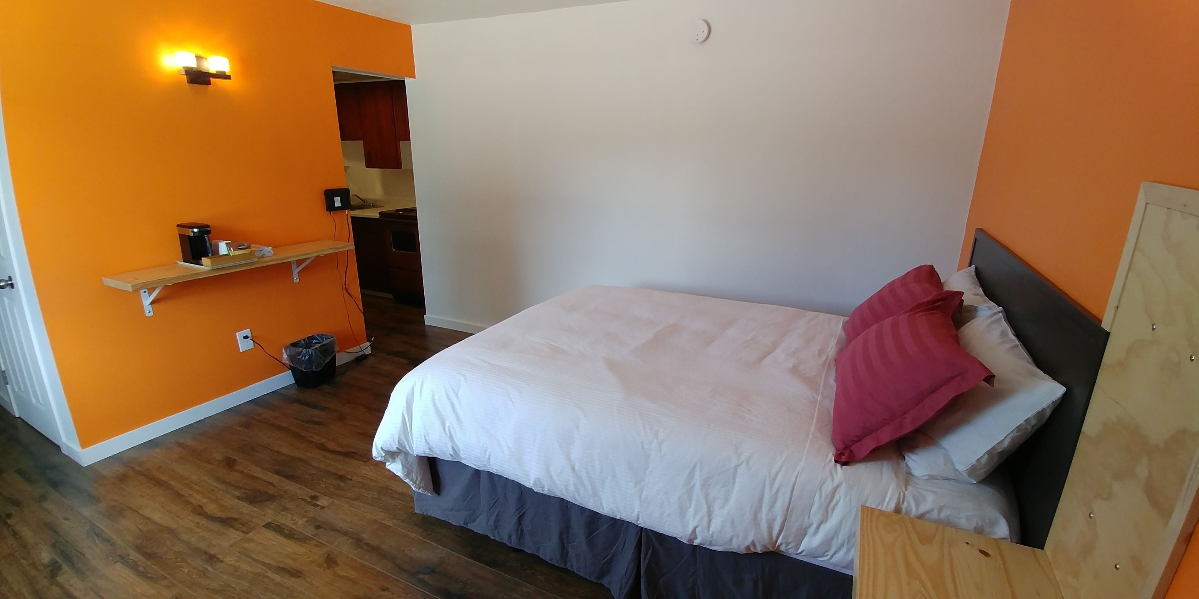 A bedroom with a bed, a wooden headboard, a shelf with items, and a wall-mounted light fixture.